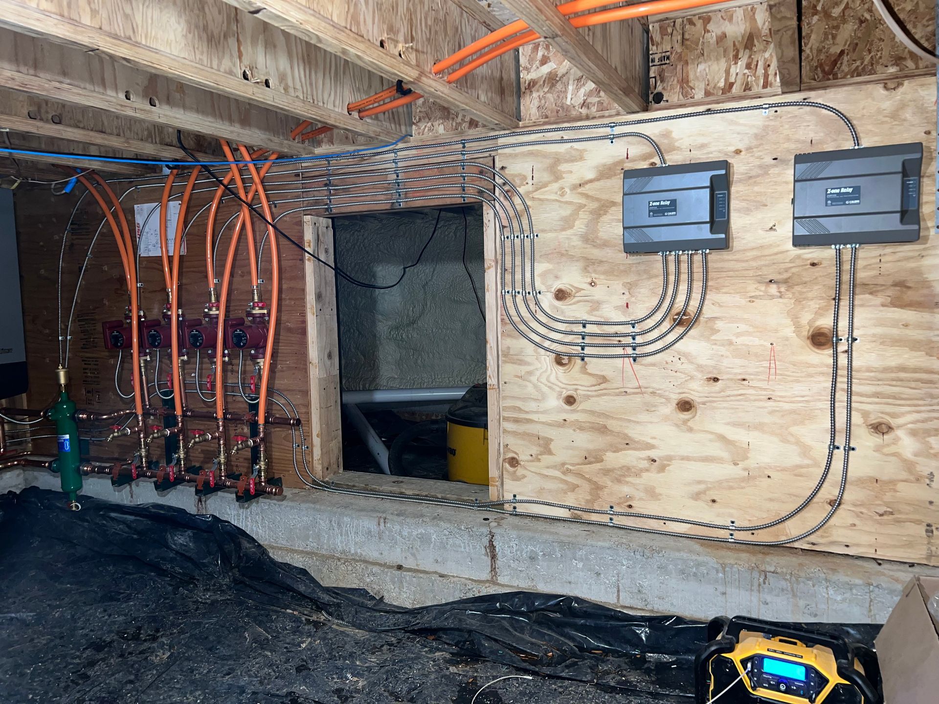 Construction site with exposed wiring, electrical panels, and plywood-covered wall openings indoors