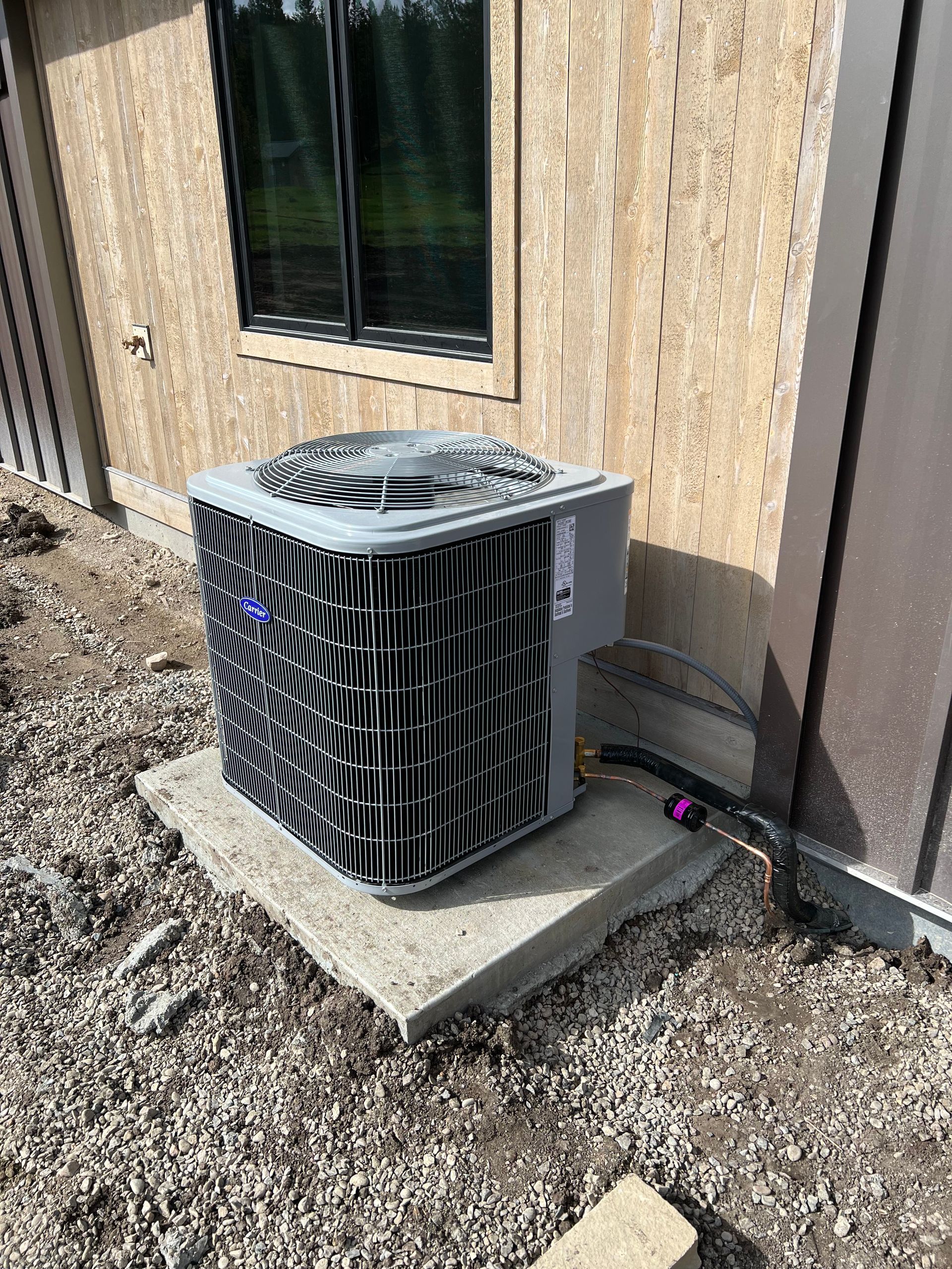 Outdoor HVAC unit beside a tan house wall on a concrete pad with gravel around it.