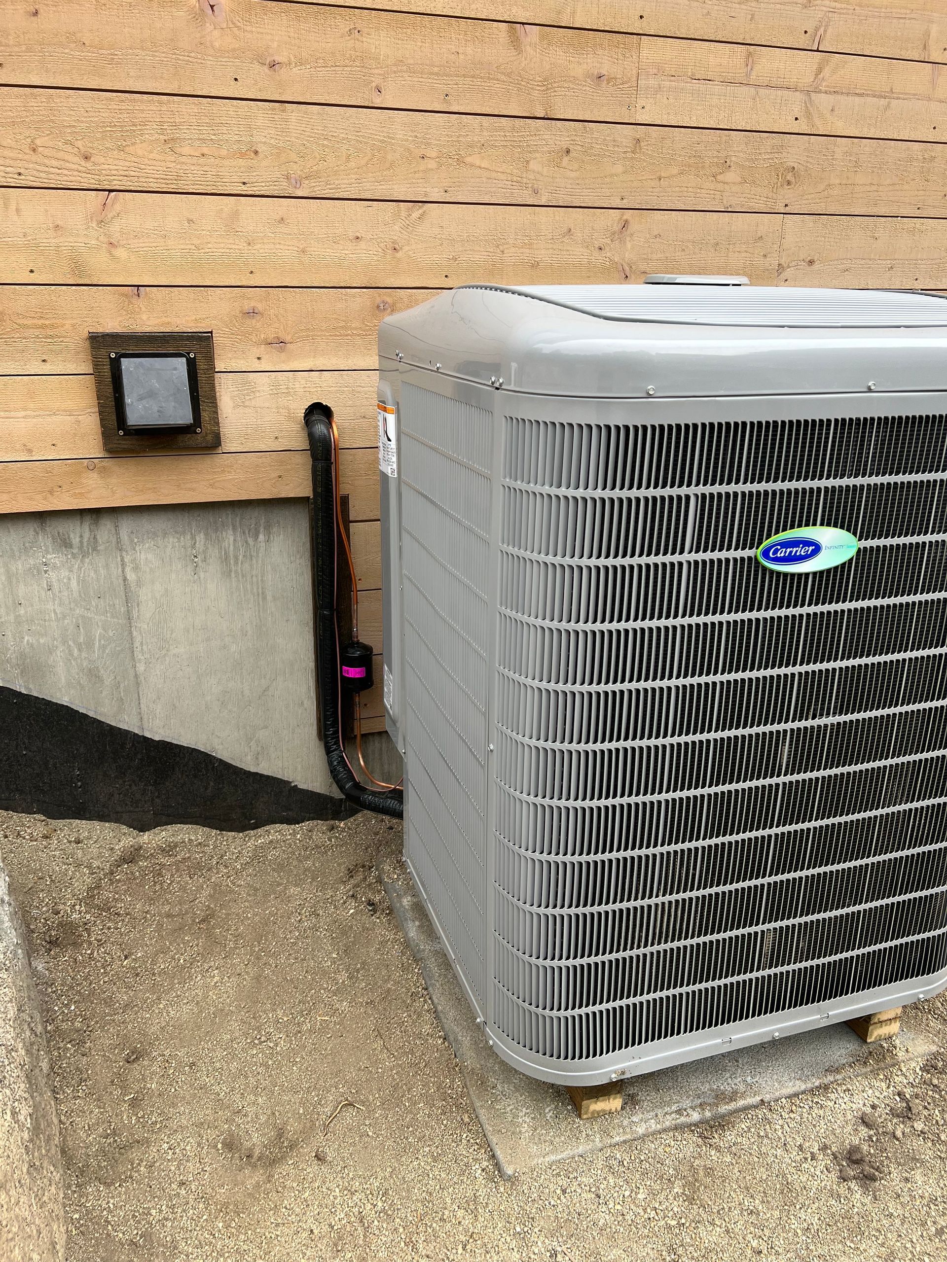 Outdoor HVAC unit beside a house wall, with a small wall light and gravel ground nearby.