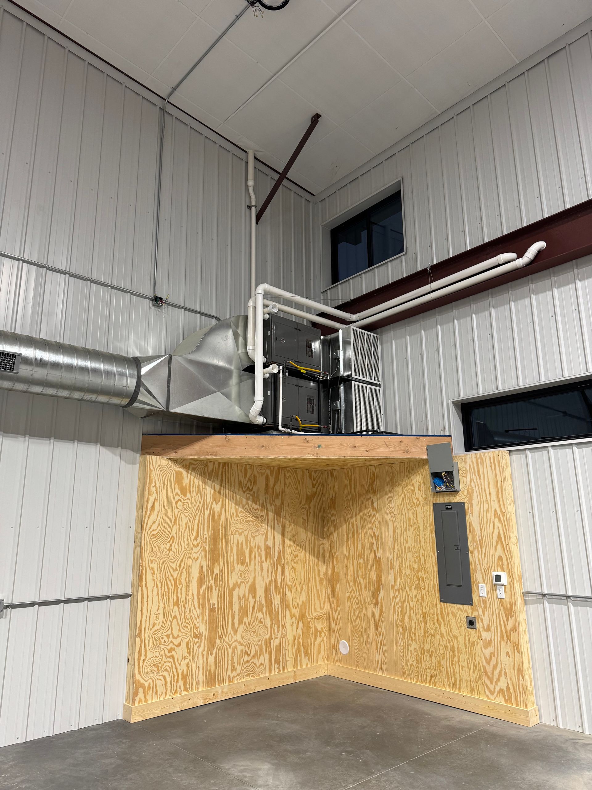 Industrial loft interior with plywood walls, metal ducting, and a catwalk/railing near the ceiling.