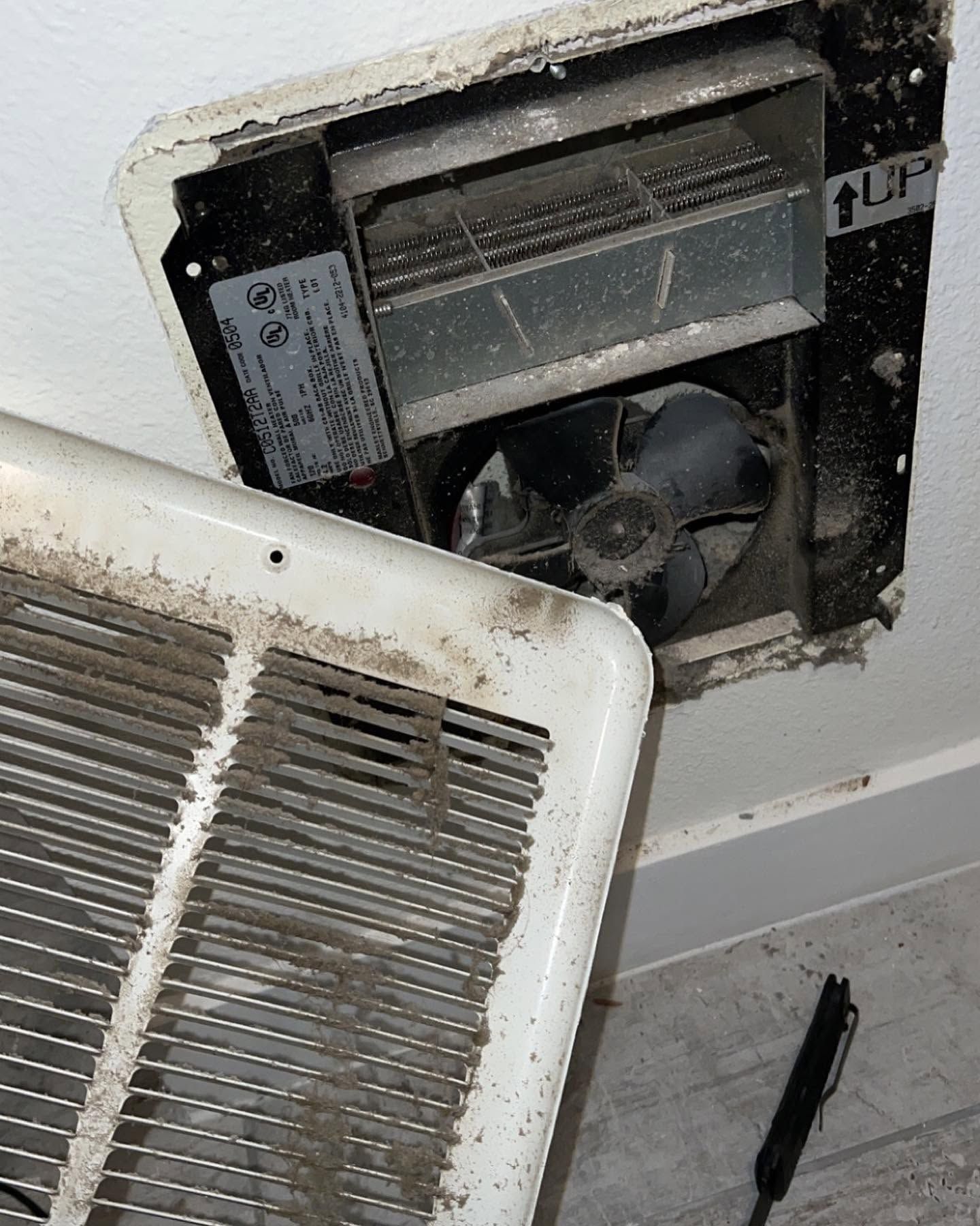 Open wall vent with a dirty white cover removed, exposing fan and filter inside.