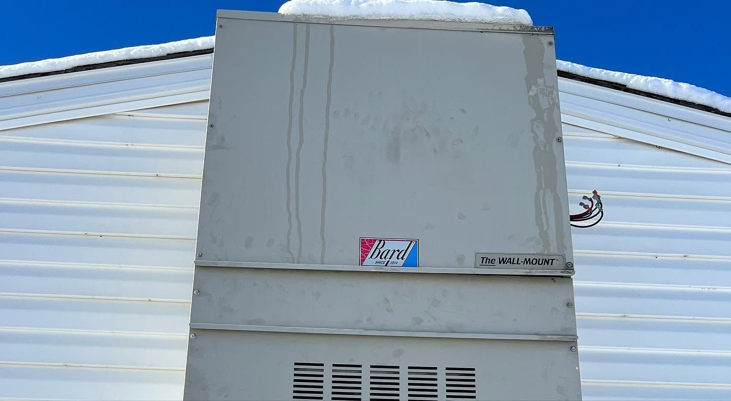 Gray rooftop HVAC unit against a white metal building under a blue sky