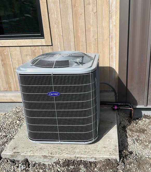 Outdoor air conditioner unit beside a tan wooden wall on a gravel pad