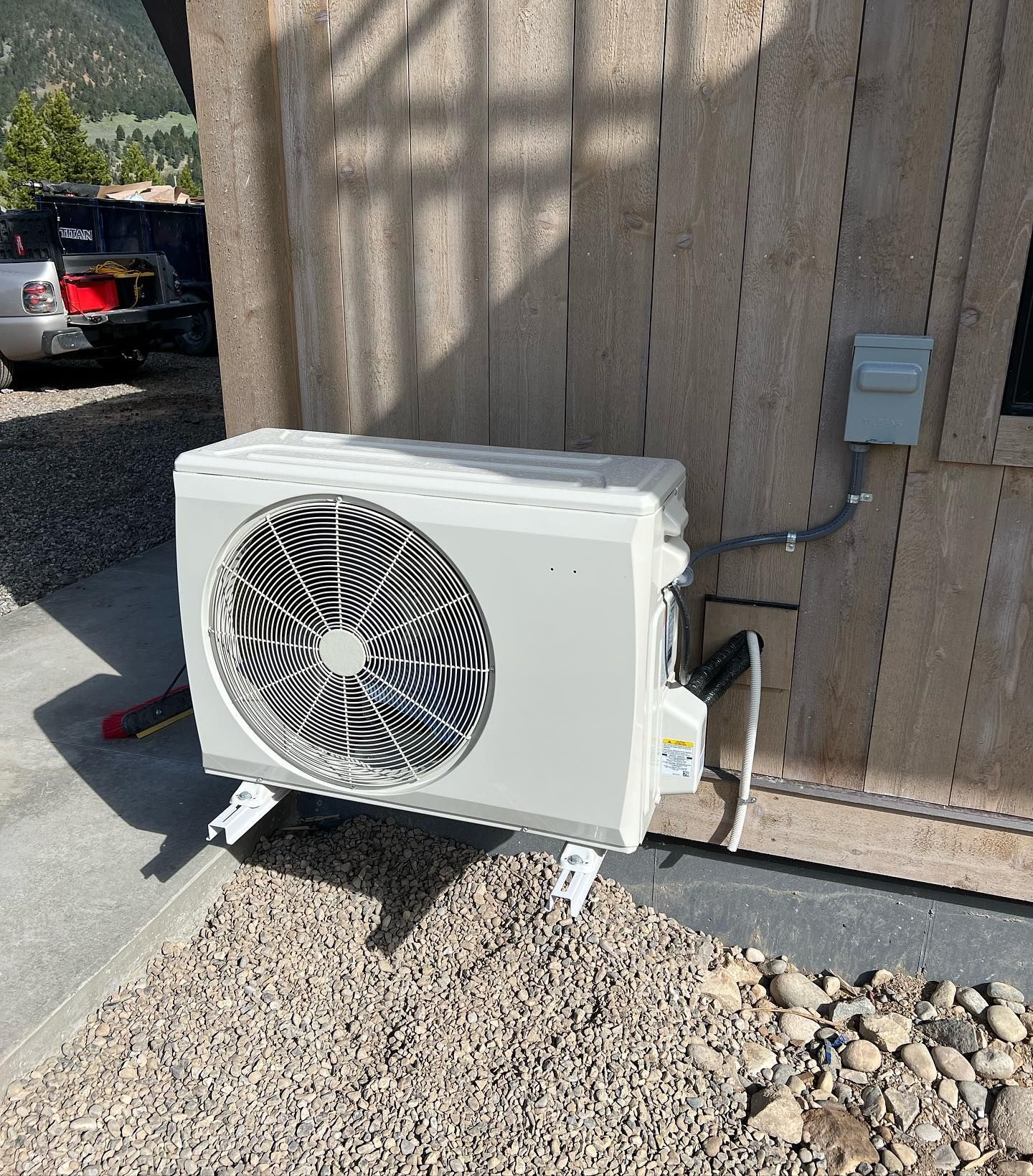 Outdoor white air conditioner unit mounted on a beige wall beside a driveway and gravel bed
