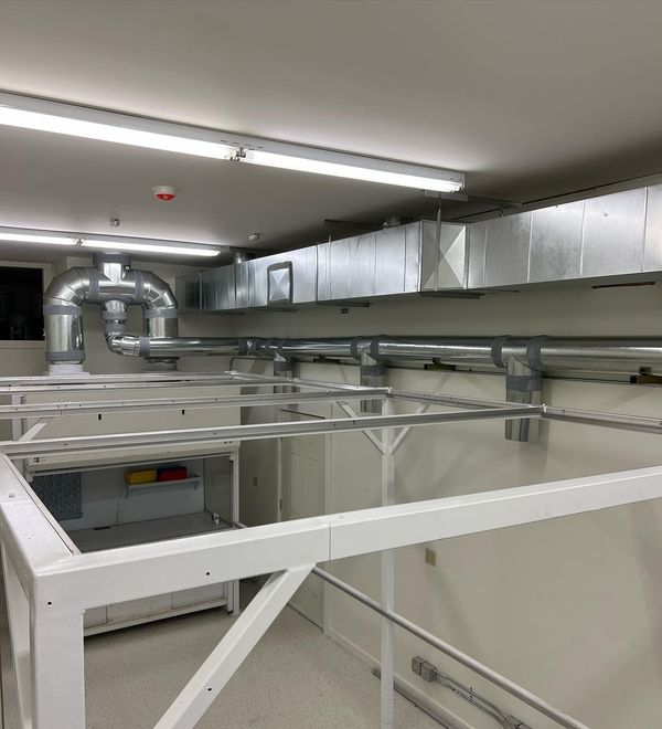 Industrial utility room with exposed silver ducts, white beams, and fluorescent ceiling lights