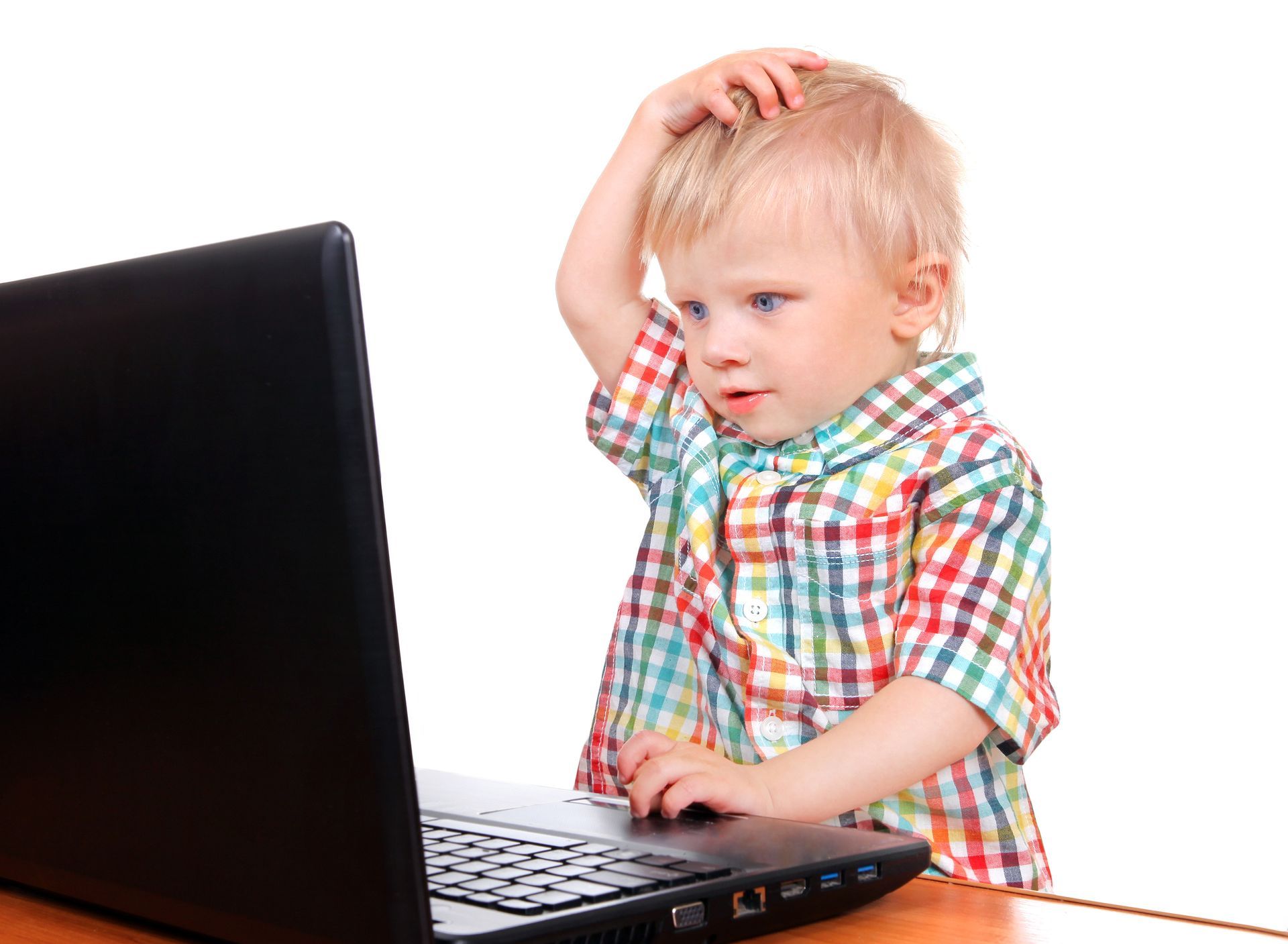 Blond toddler with puzzled expression touching head while looking at a laptop.