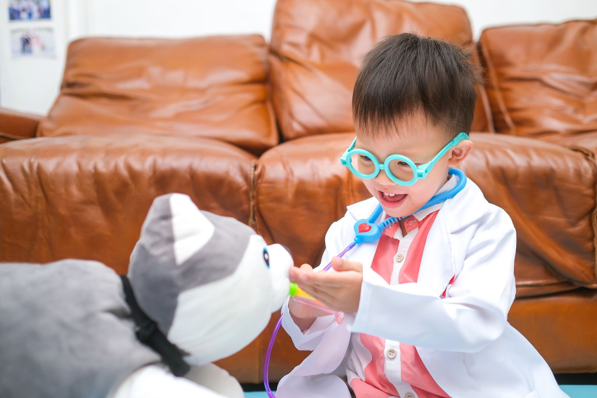 A little boy is dressed as a doctor and playing with a stuffed animal.