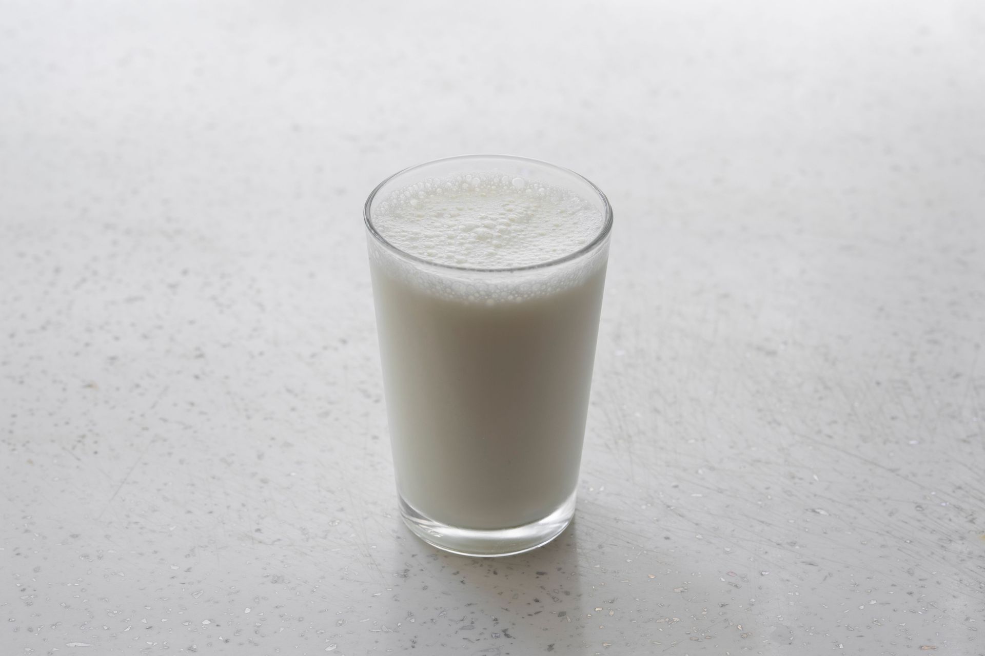 A clear glass of milk on a light speckled countertop.