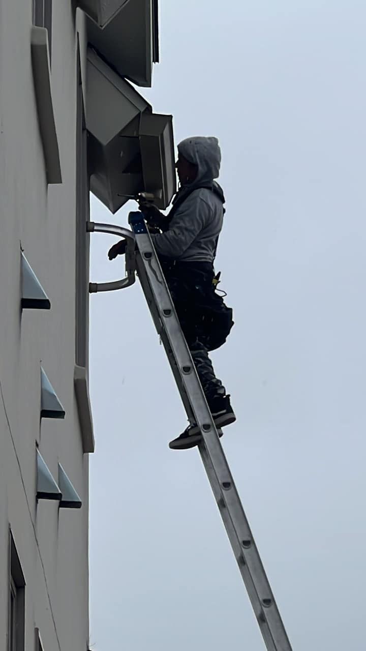 A man is standing on a ladder on the side of a building.