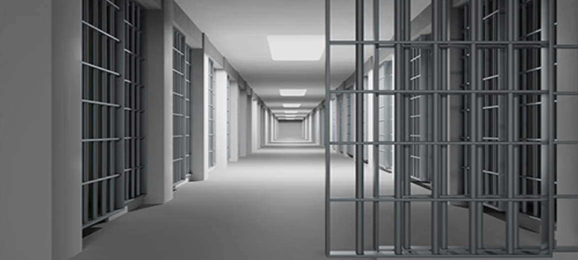 Empty jail corridor with barred cell doors lining both sides under fluorescent lights