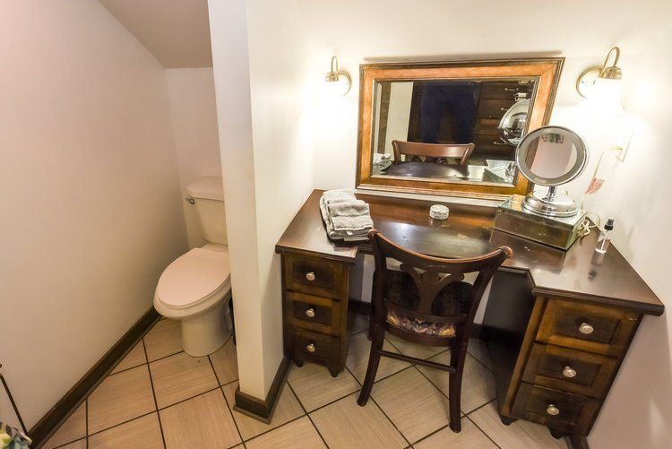 Vanity area with a toilet visible, featuring a wooden desk, mirror, and chair in a small room.