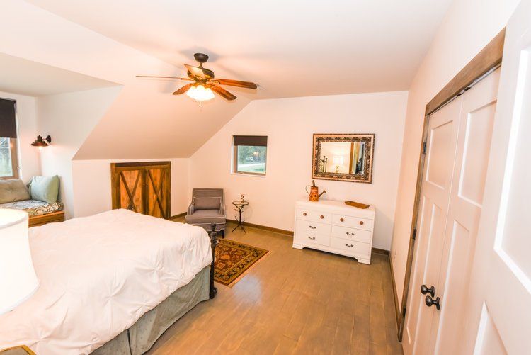 Bedroom with bed, dresser, chair, window, and barn door; neutral tones and wooden accents.