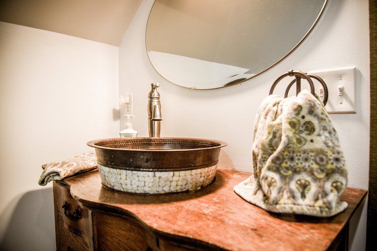 Rustic bathroom sink with bronze faucet, oval mirror, wooden cabinet, and decorative hand towel.