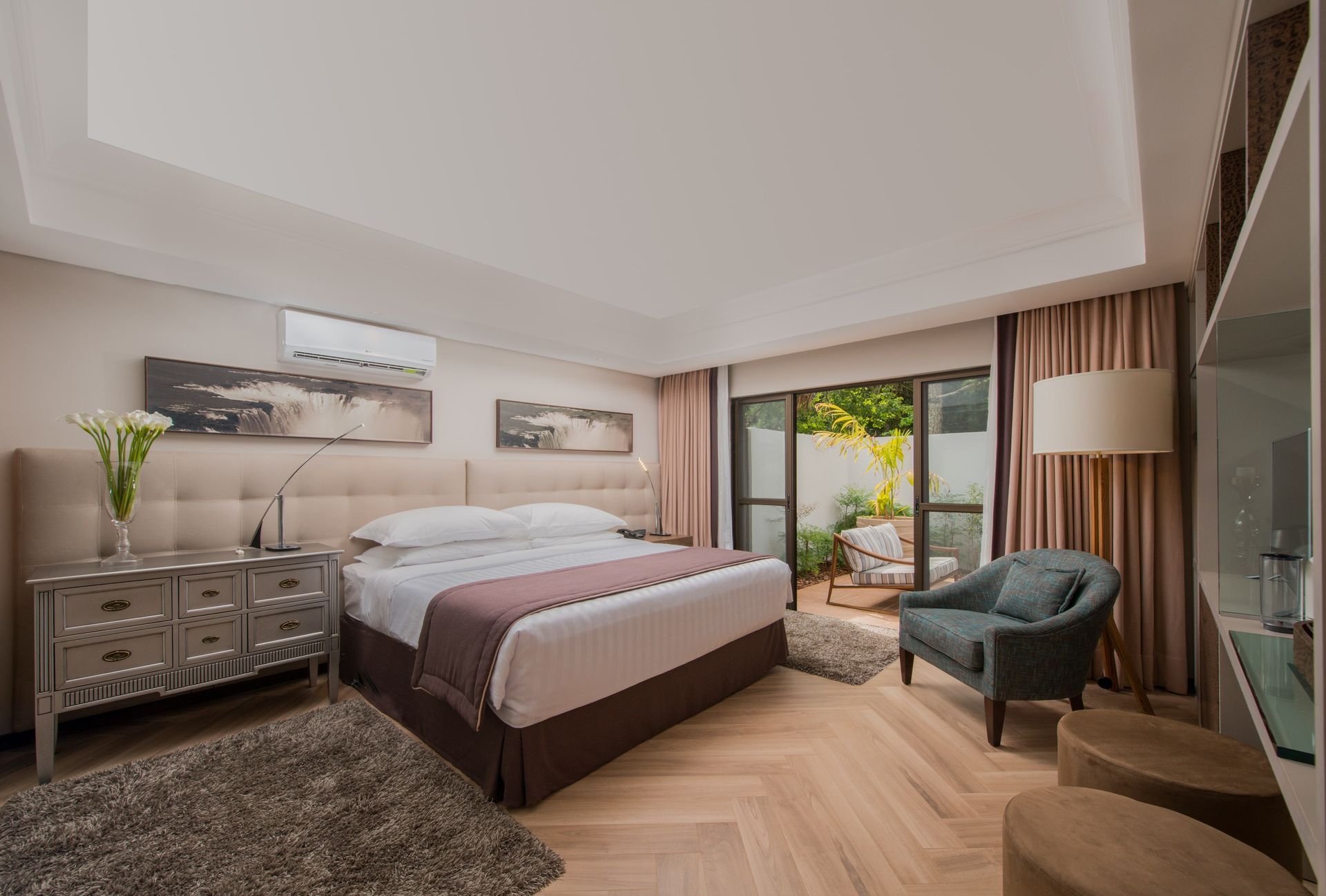 Um quarto de hotel com uma cama king size, cadeiras, cômoda e portas de vidro deslizantes.