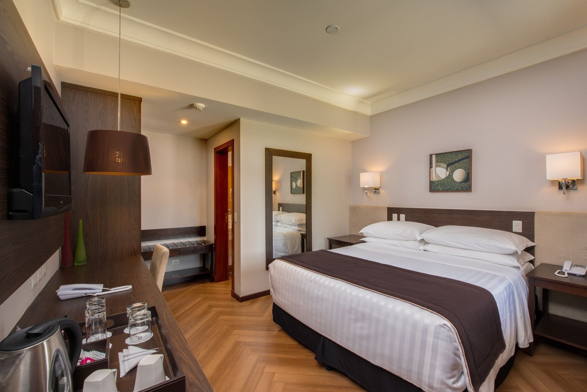 Um quarto de hotel com uma cama king size, escrivaninha, televisão e espelho.