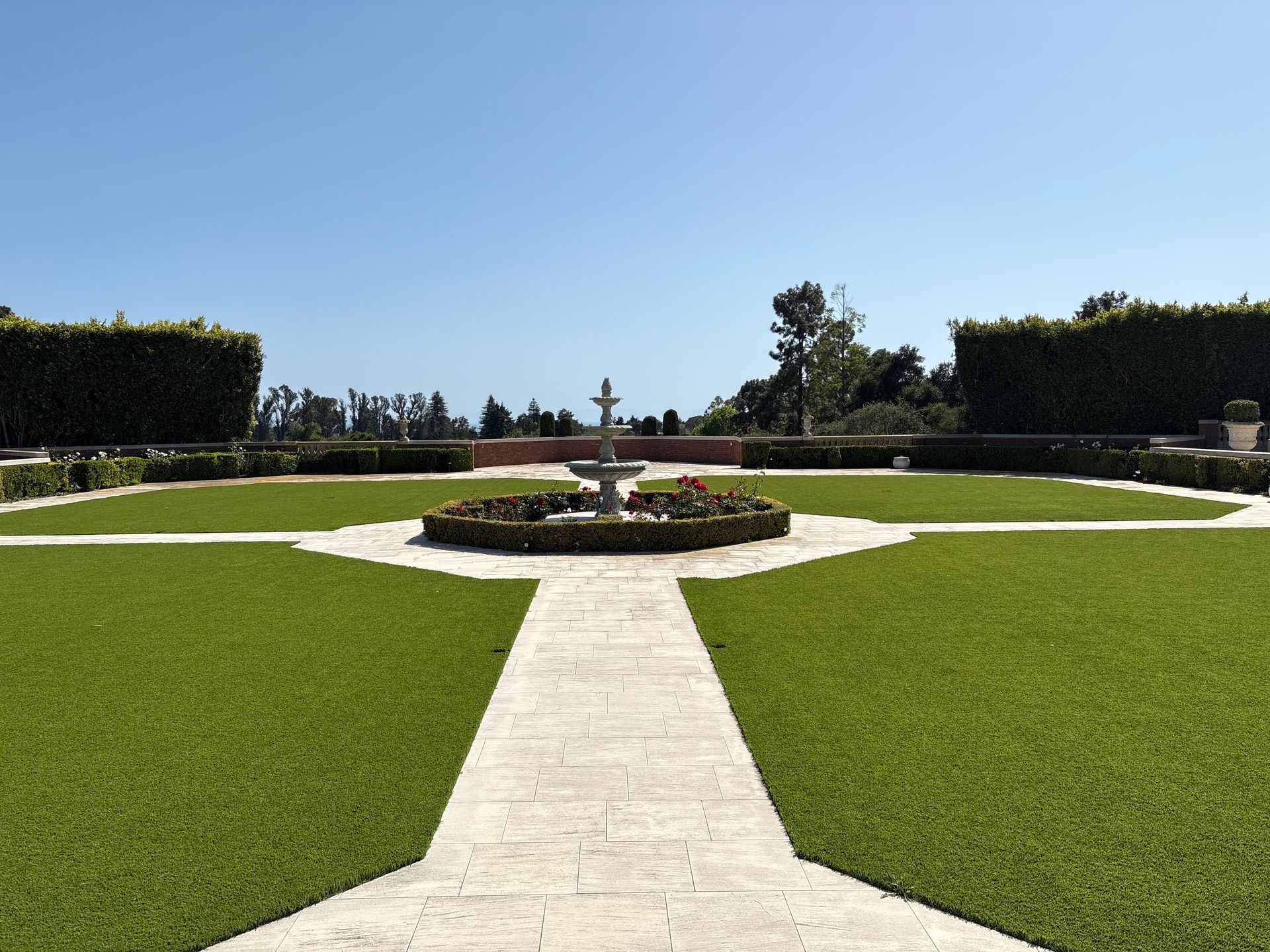 Formal garden with a stone walkway leading to a circular flower bed and manicured green lawns under a clear sky