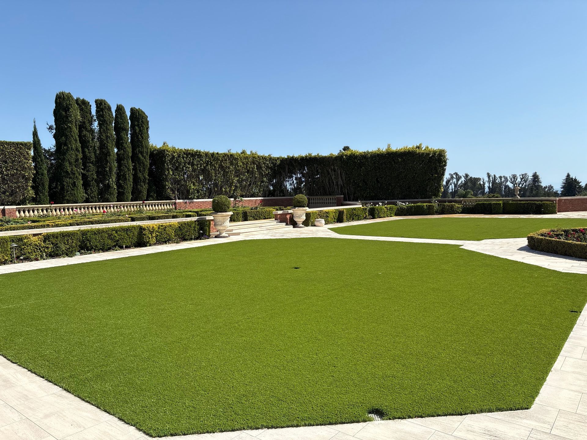 Formal garden with green lawn, hedges, and stone paths under a clear blue sky