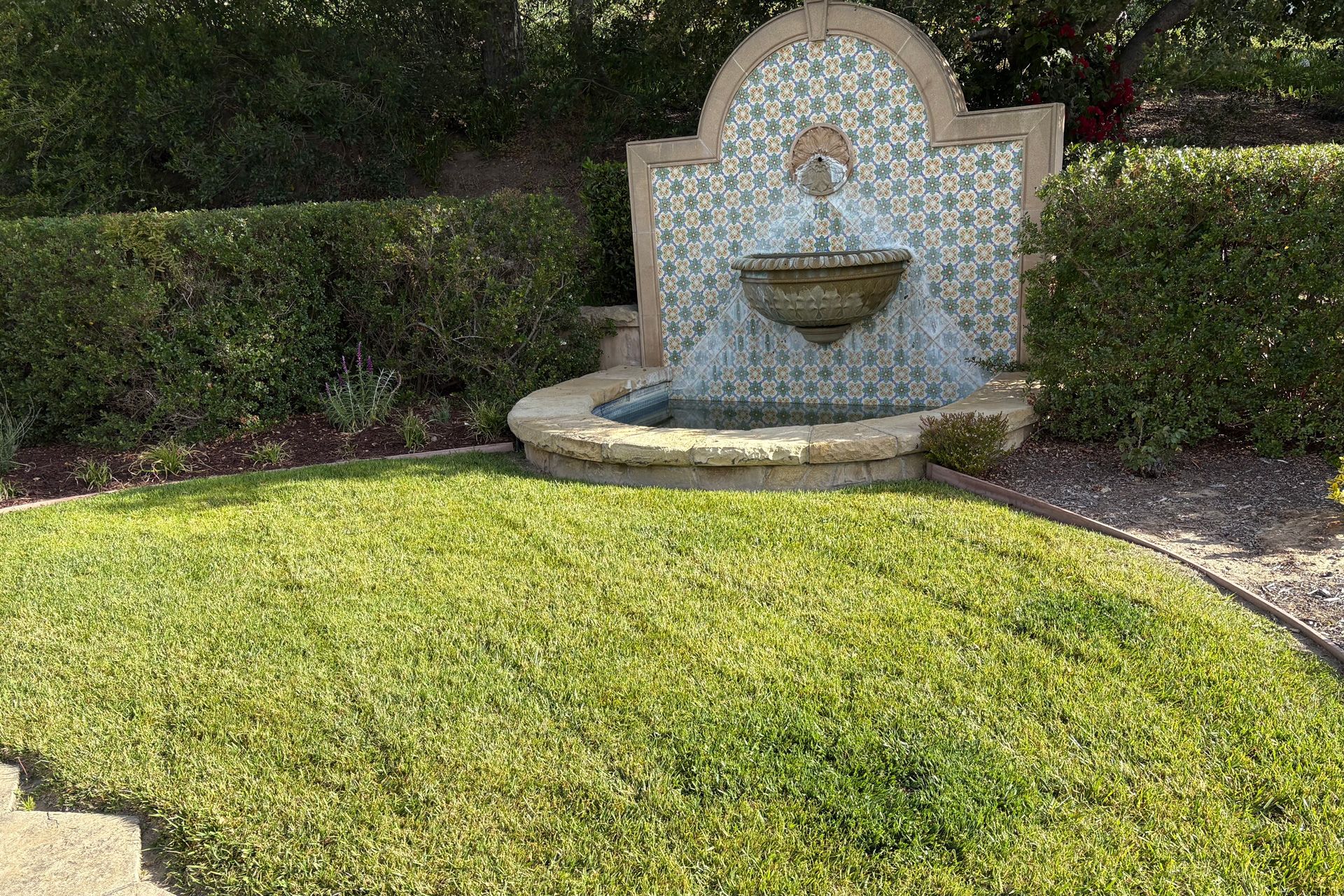Decorative tiled fountain set in a manicured garden beside a green lawn and hedges