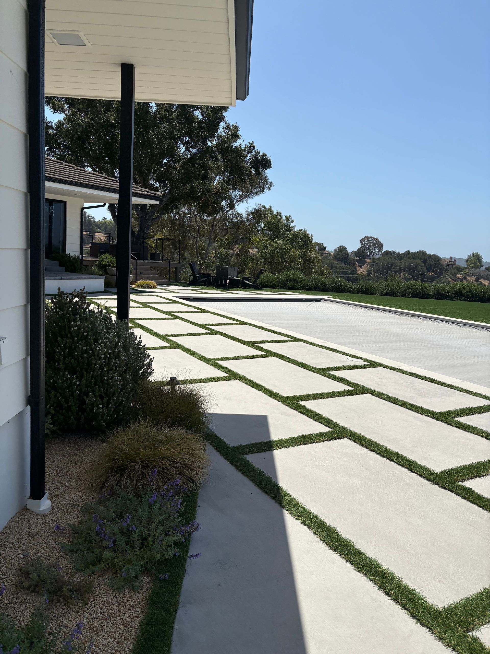 Modern house exterior with a sunny driveway of white pavers and green grass strips.