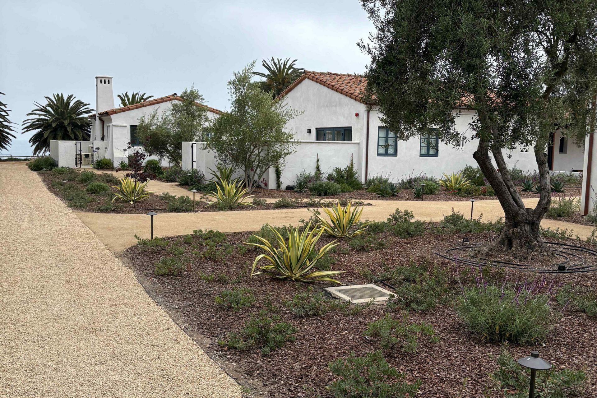 White house with red roof and desert landscaping beside a gravel driveway