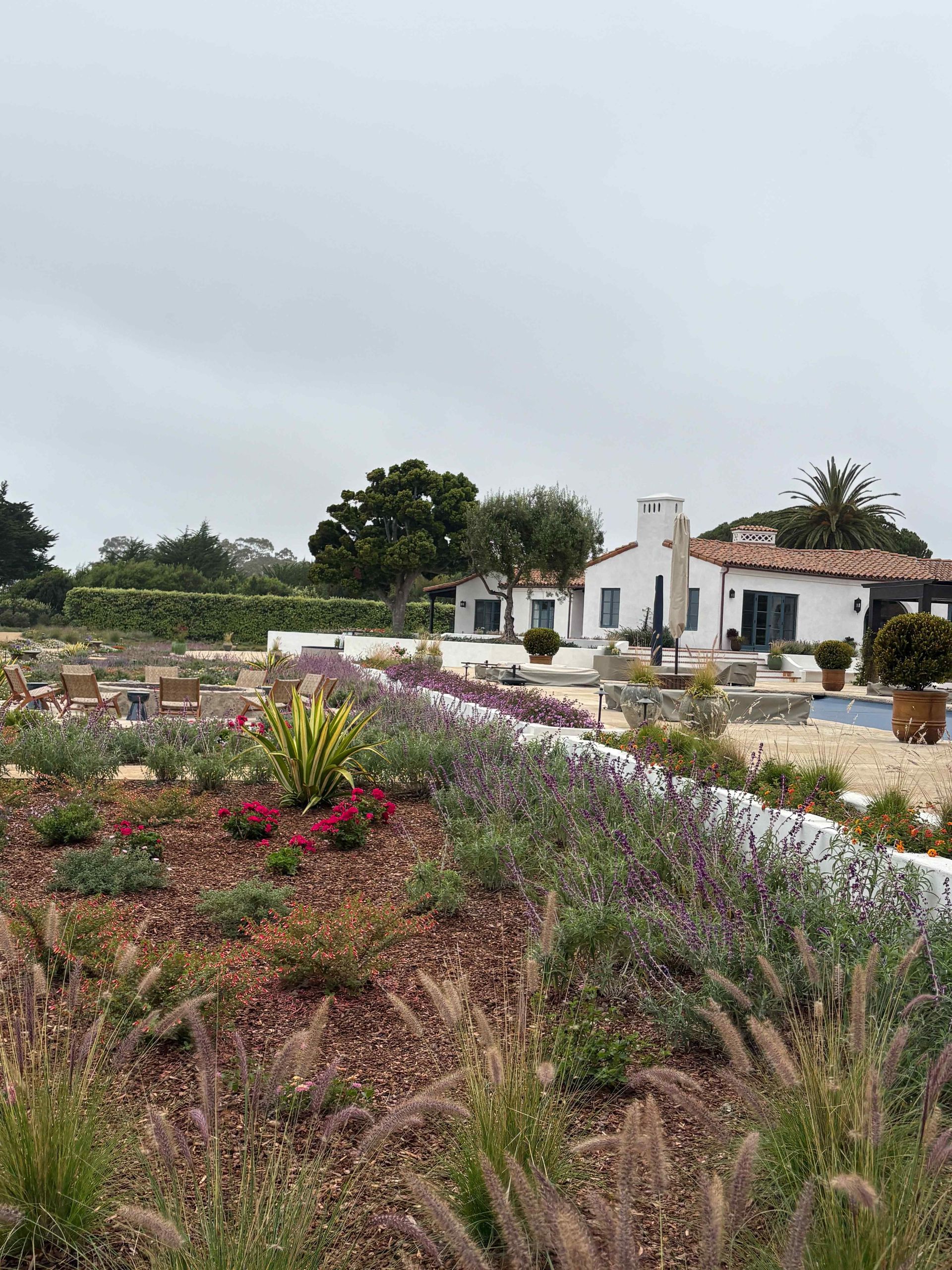 Colorful flower garden beside a white cottage under a cloudy sky