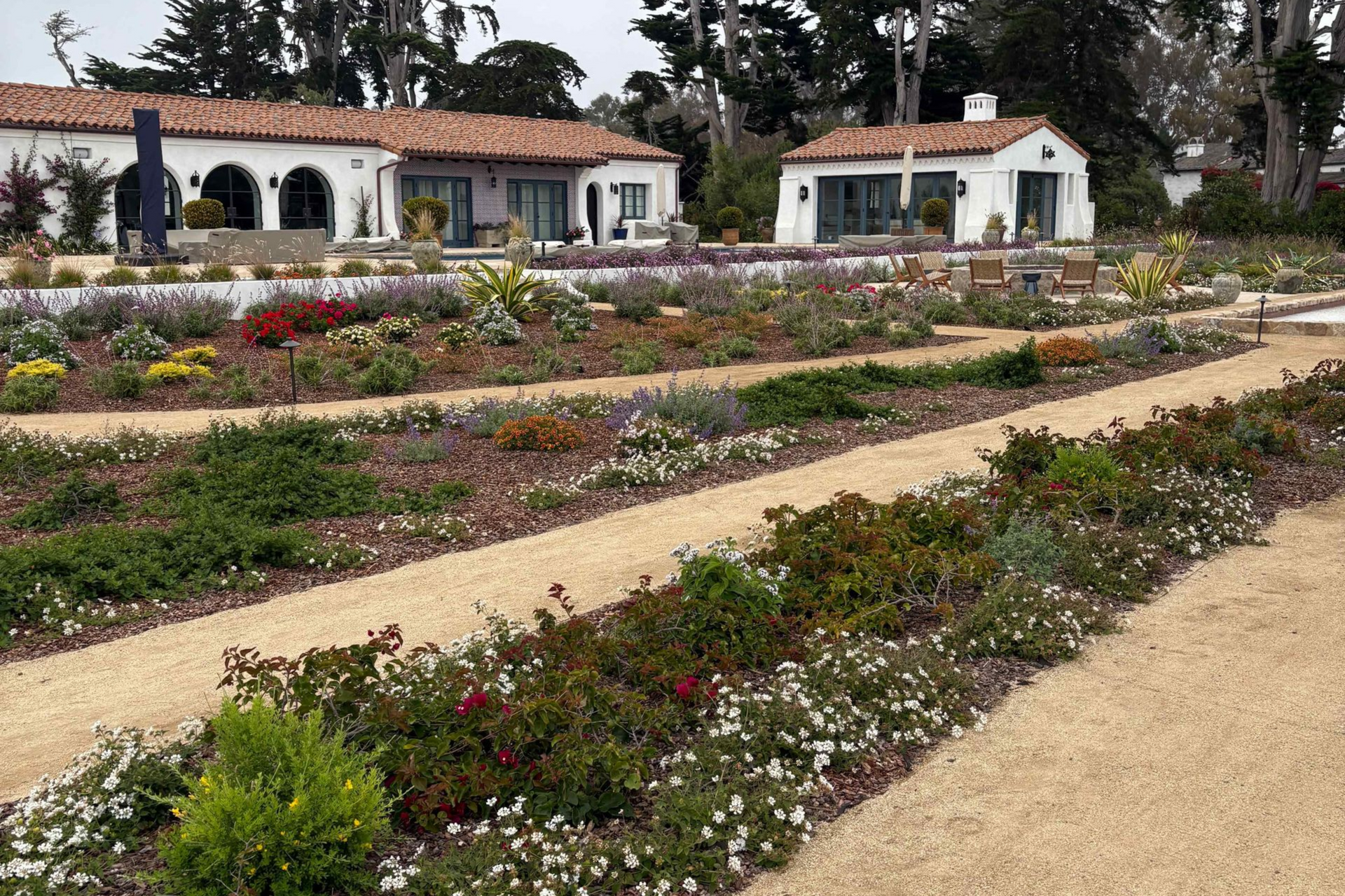 Flower garden with winding gravel paths and white cottages under trees