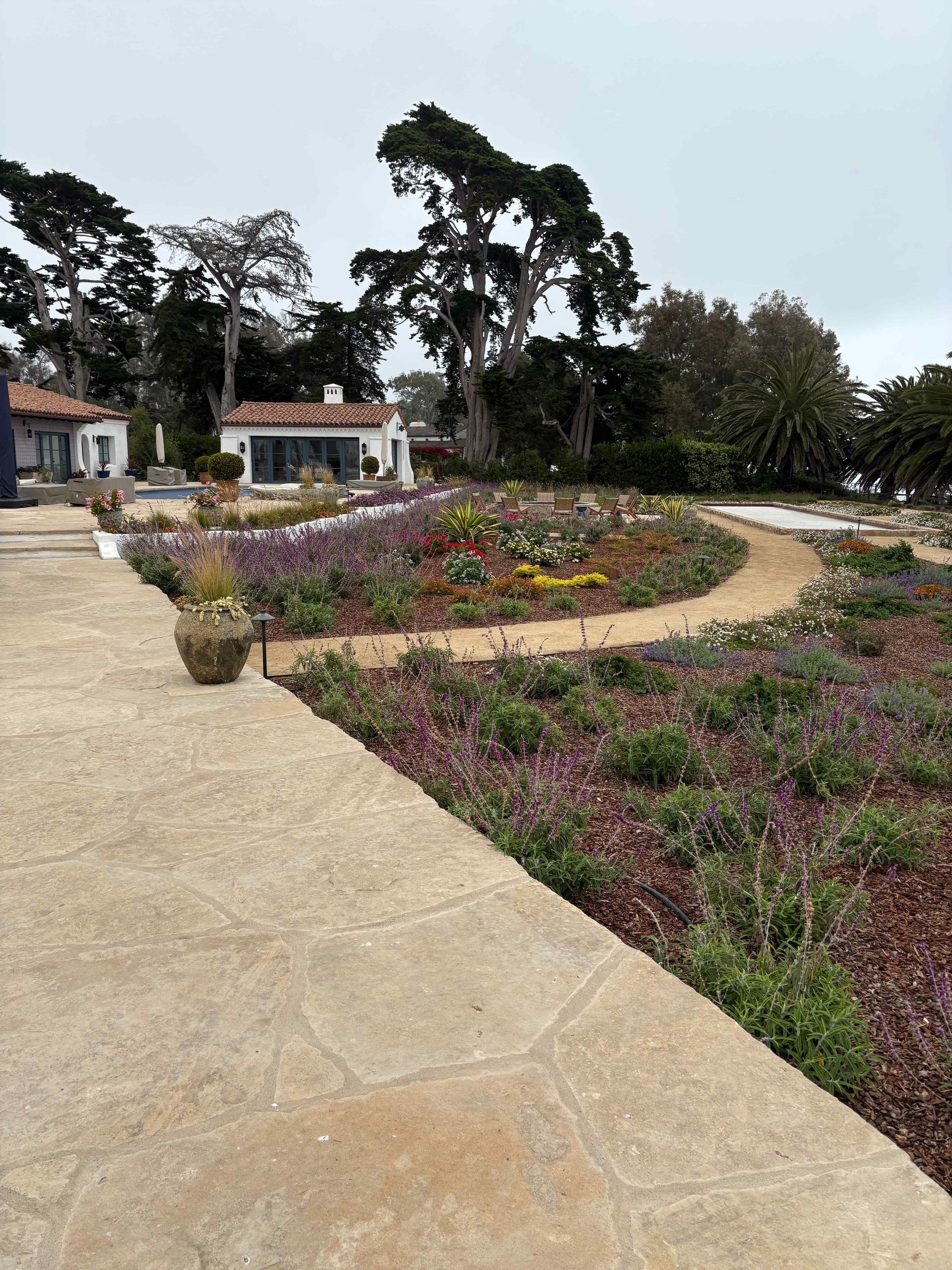 Curved garden path beside colorful flower beds and tall trees in a park