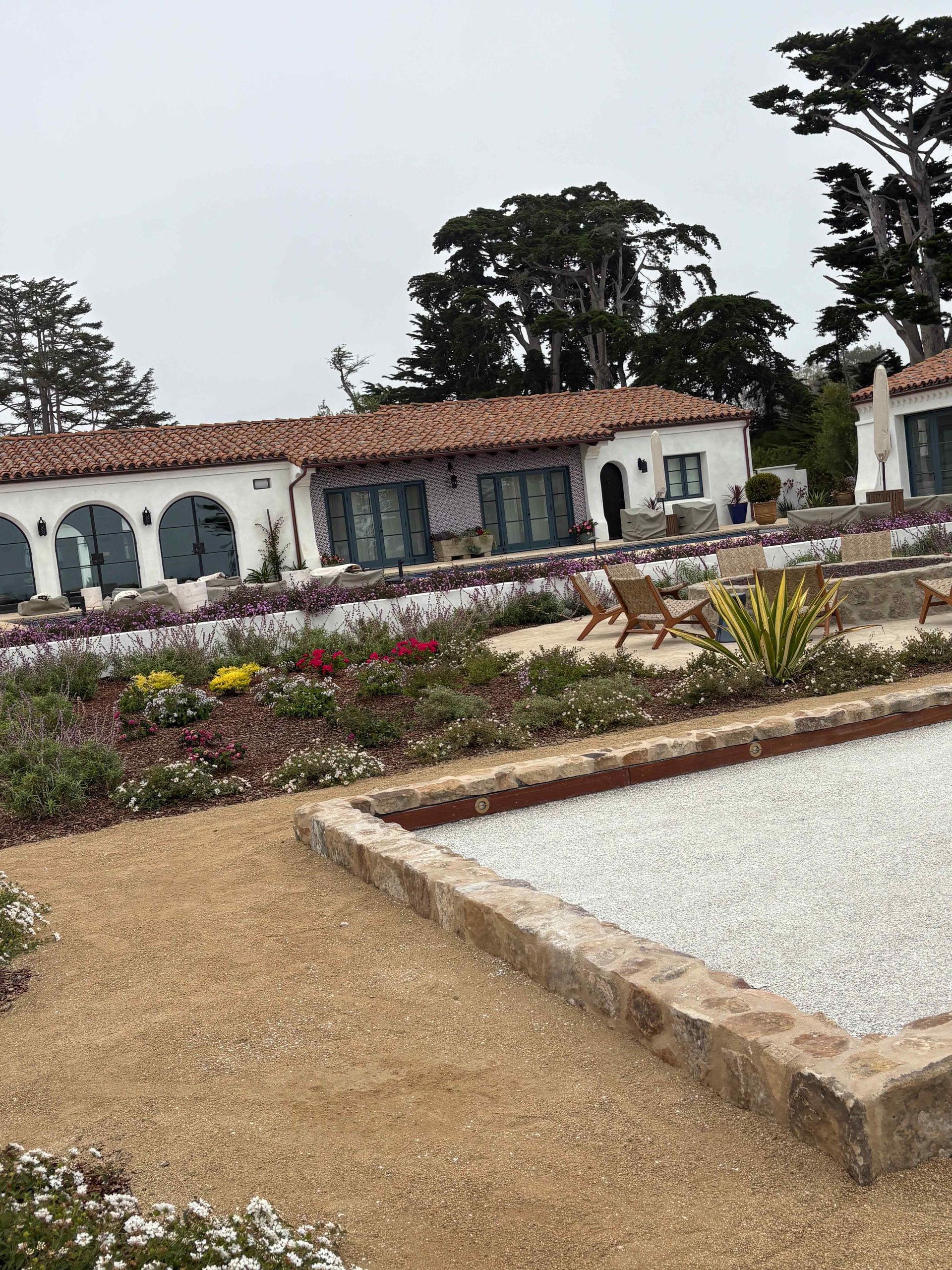 Landscaped garden with gravel paths, flower beds, and a white building with arches in the background