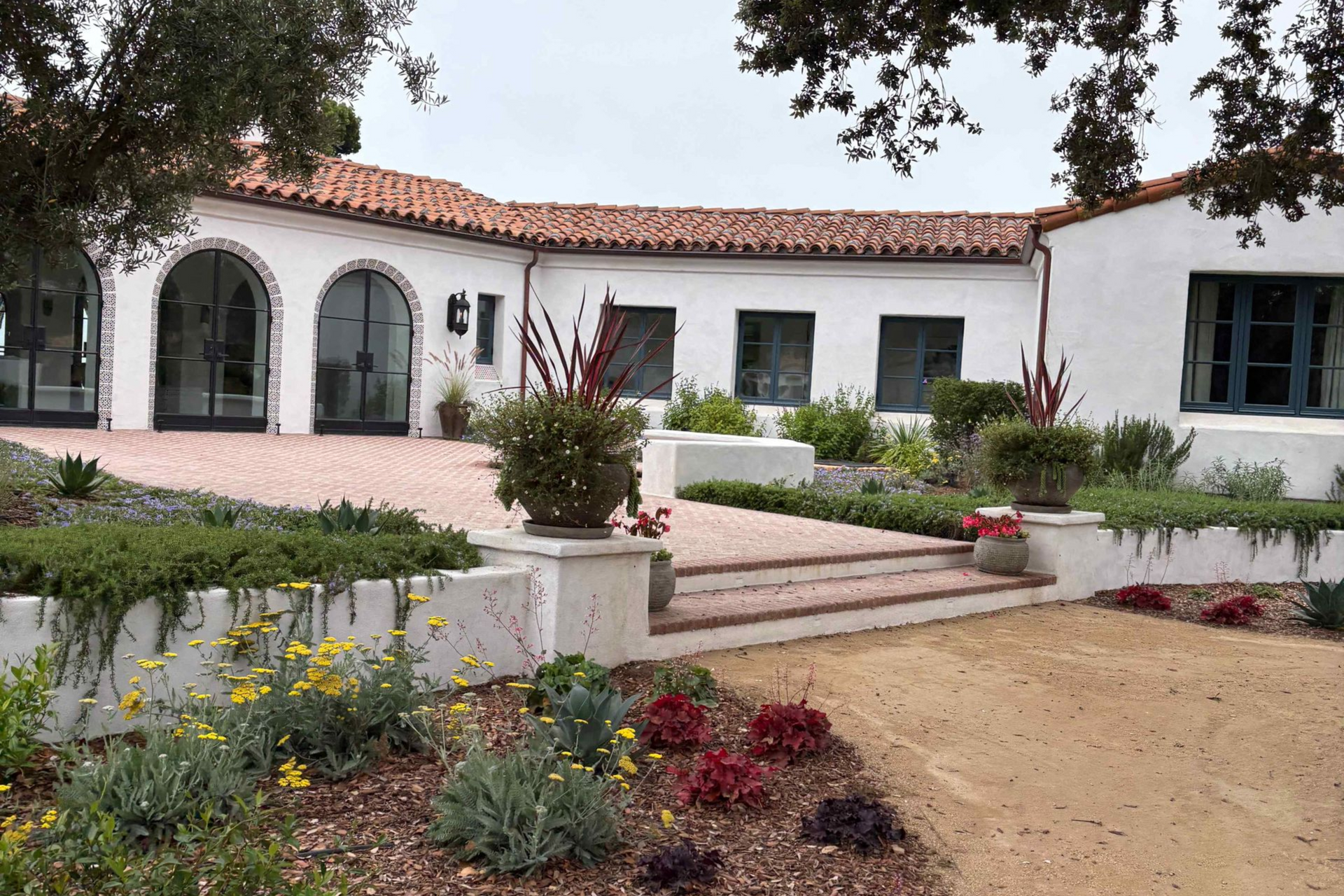 White stucco house with red tile roof, arched windows, and a landscaped front garden with steps.