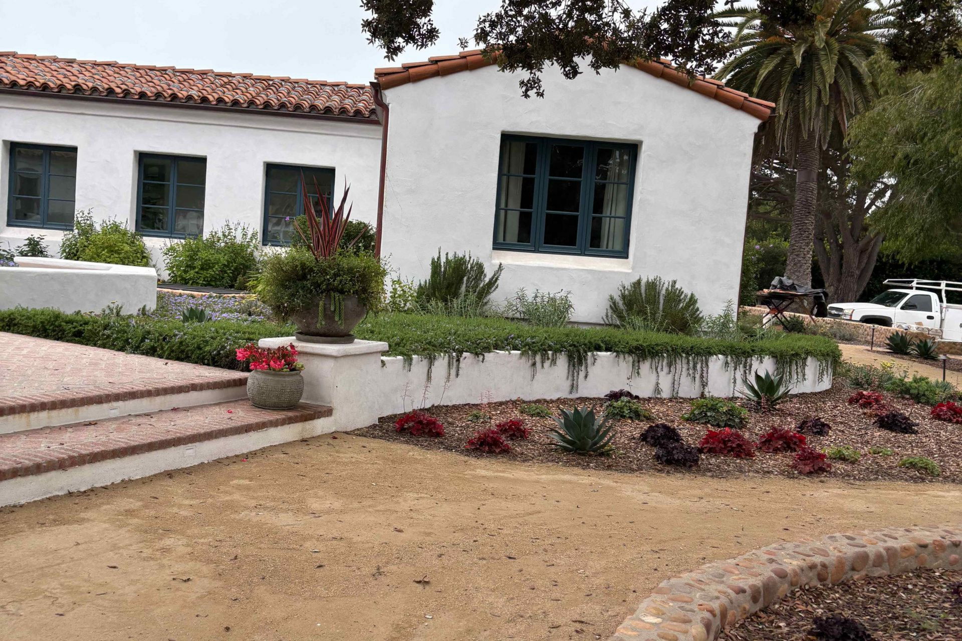 White stucco house with green-trimmed windows, red tile roof, and landscaped flower beds in front