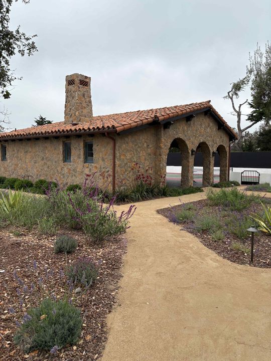 Adobe-style house with arched porch, gravel path, and desert landscaping under a cloudy sky
