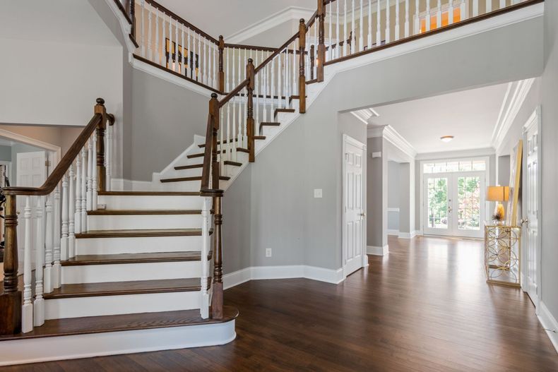 Bright foyer with wood floors, staircase, and railing leading to an open hallway and windows.