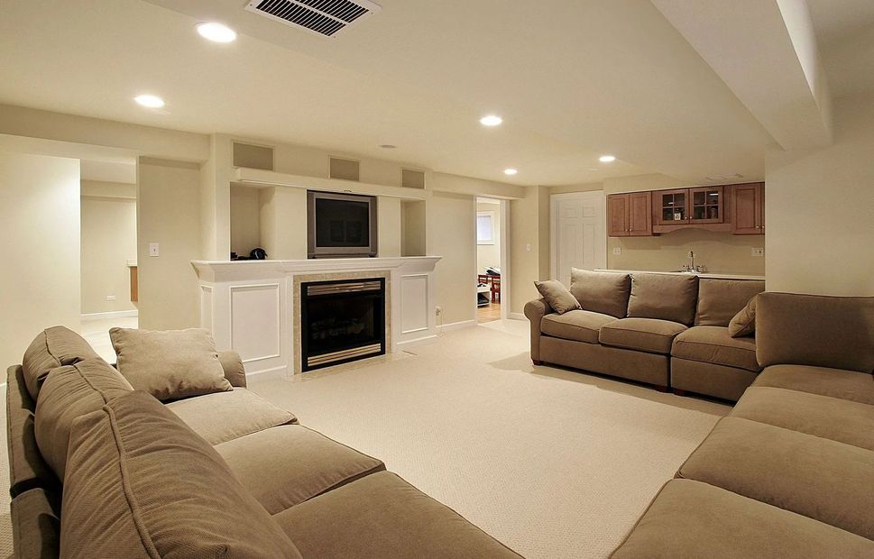 Spacious beige living room with sectional sofas, fireplace, wall-mounted TV, and soft recessed lighting