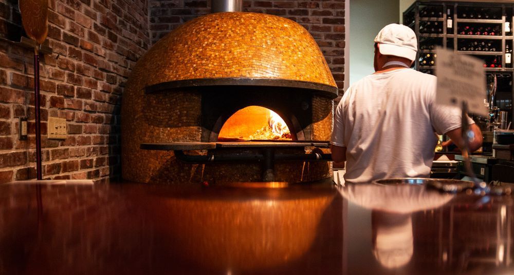 A Man is Standing in Front of a Large Pizza Oven — Michelangelos Pizza & Pasta in Aitkenvale, NSW