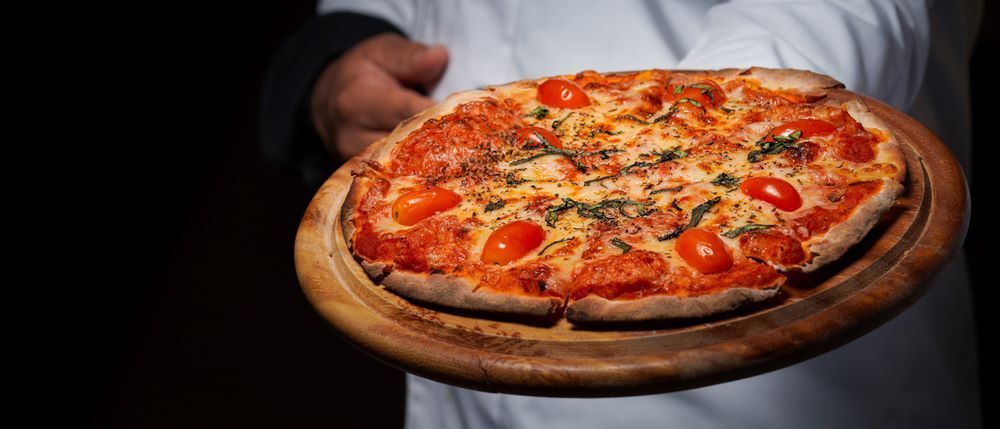 A Man is Holding a Pizza on a Wooden Cutting Board — Michelangelos Pizza & Pasta in Hermit Park, QLD