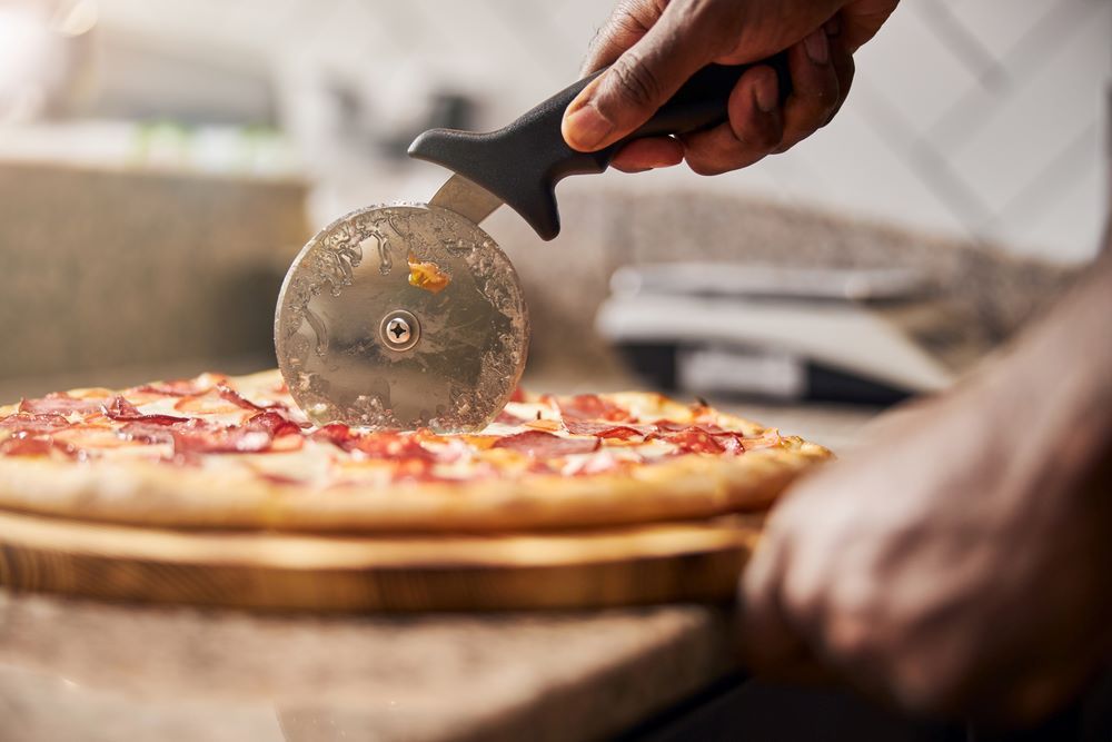 A Person is Cutting a Pizza With a Pizza Cutter — Michelangelos Pizza & Pasta in Kirwan, QLD