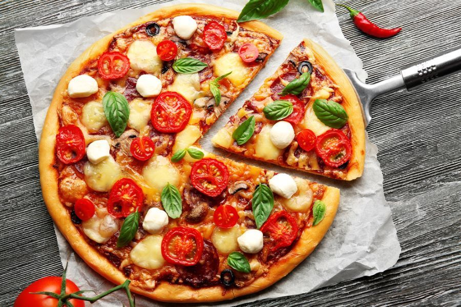 A Pizza With Tomatoes , Mozzarella , Basil and Pepperoni is on a Table With a Slice Taken Out of It — Michelangelos Pizza & Pasta in South Townsville, QLD