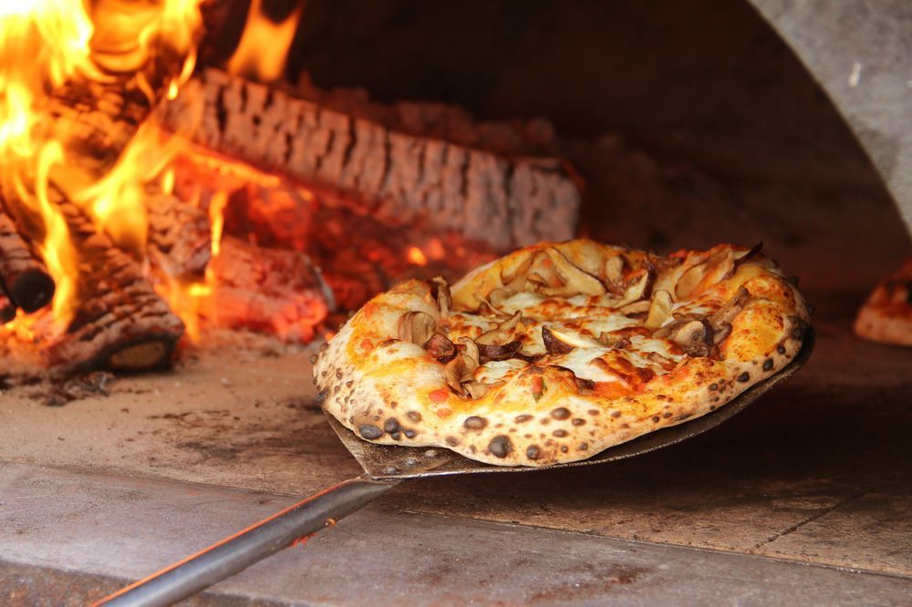 A Pizza is Being Taken Out of an Oven With a Spatula — Michelangelos Pizza & Pasta in South Townsville, QLD
