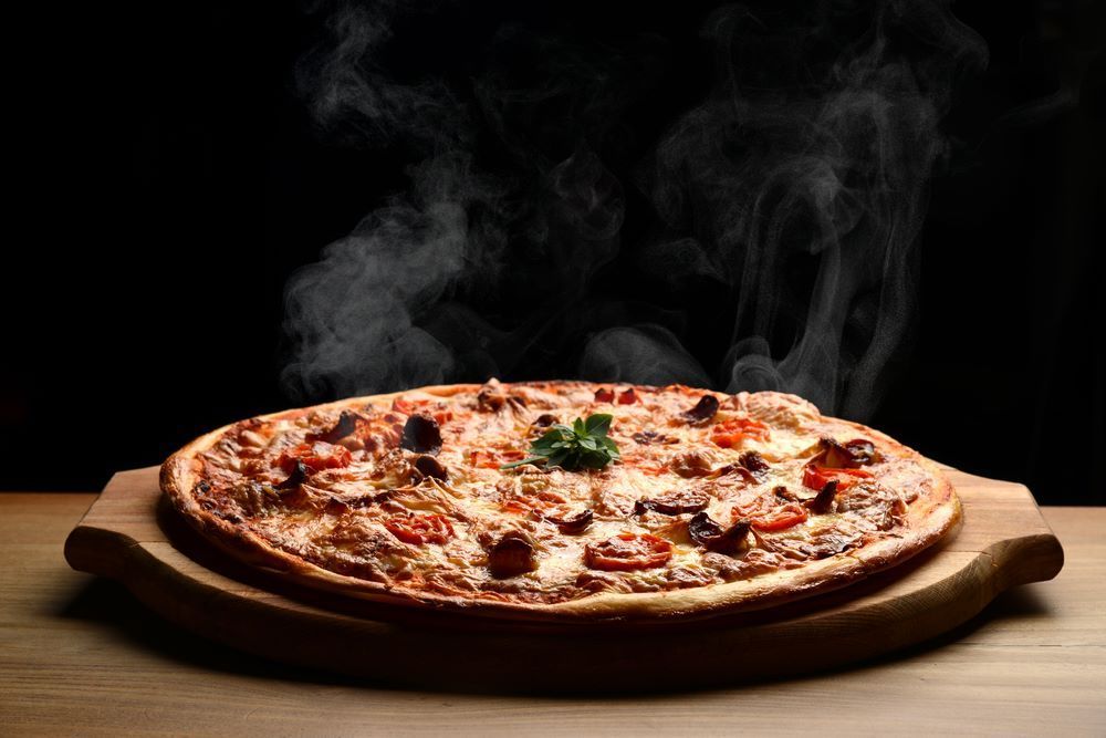 A Pizza is Sitting on a Wooden Cutting Board With Steam Coming Out of It — Michelangelos Pizza & Pasta in Burdell, QLD