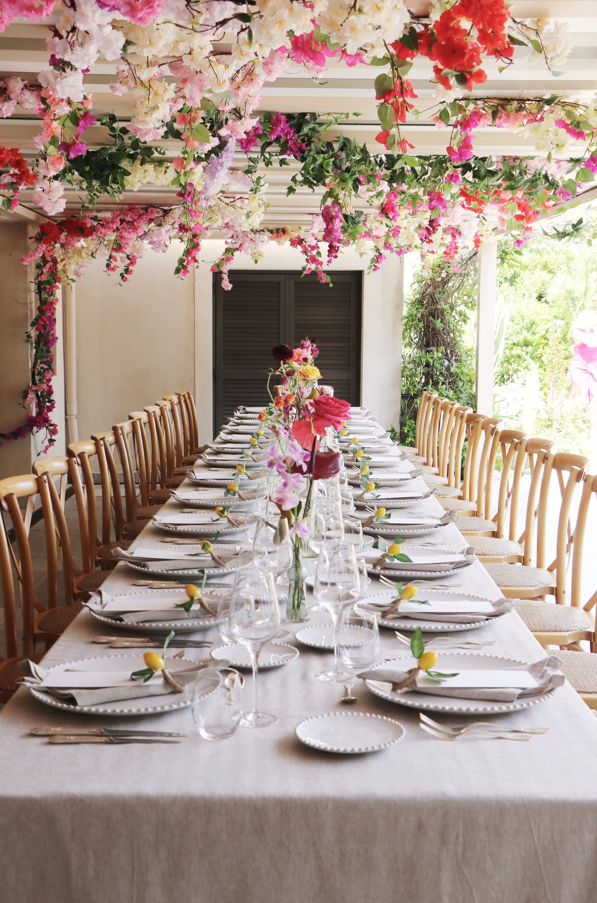 Une longue table avec des assiettes, des verres et des fleurs suspendues au plafond.