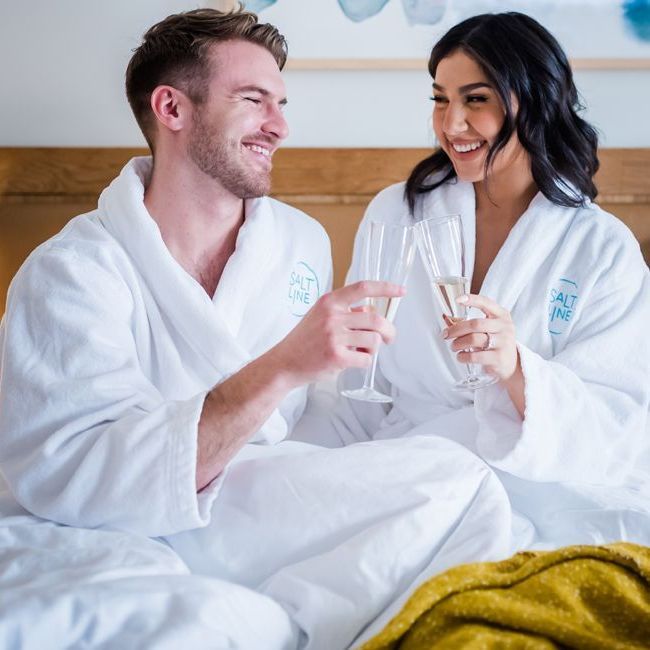 a man and a woman are sitting on a bed holding champagne glasses