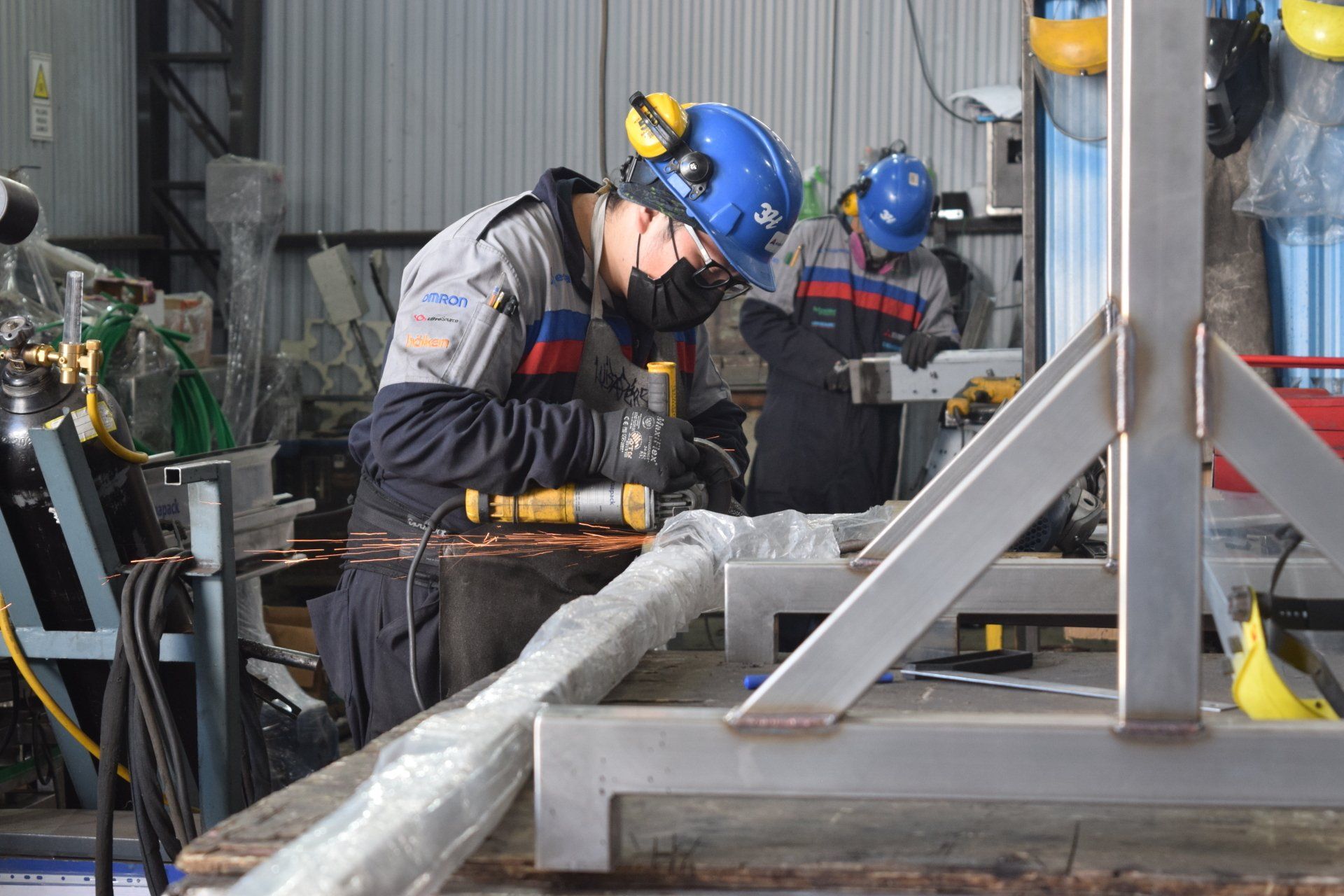 Trabajadores con cascos soldando metal en un taller industrial.