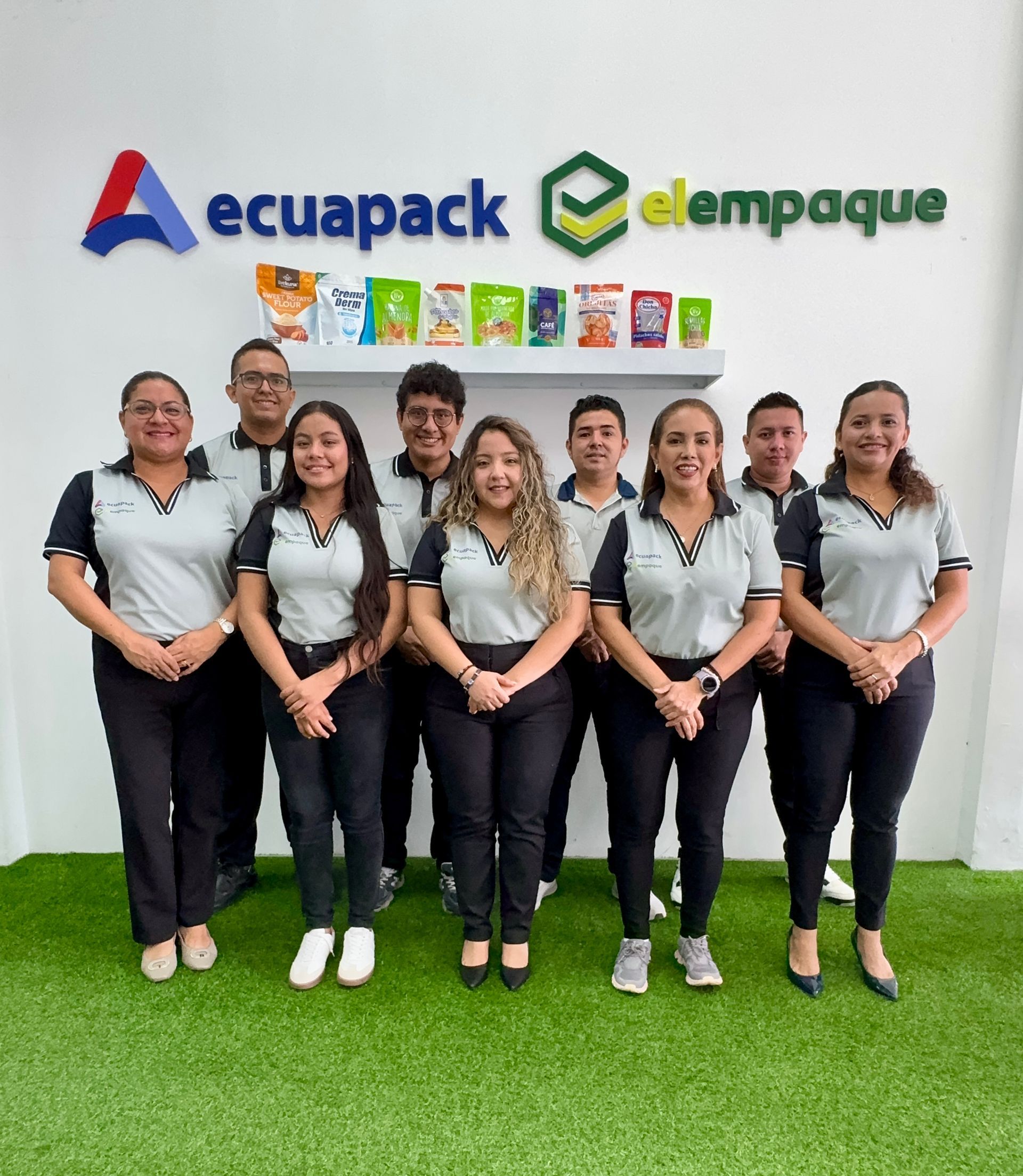 Grupo de ocho empleados posando frente a los logotipos de Asepack y Elempaque en una pared blanca.