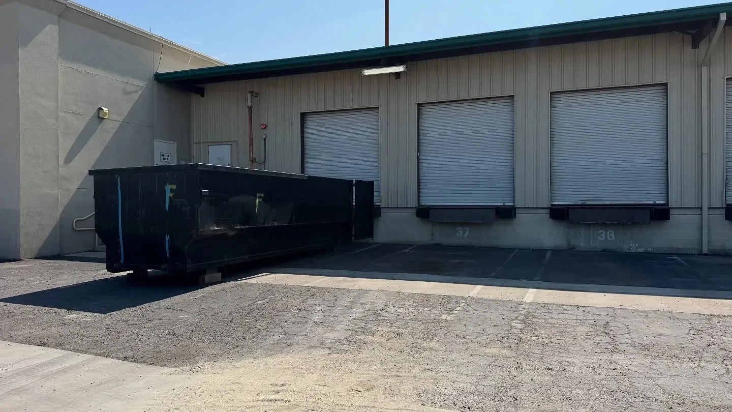 Black dumpster in front of a commercial building with three loading docks.