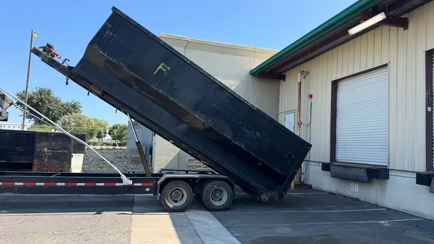 Dump truck bed tilted upwards, dumping waste near a building's loading dock.