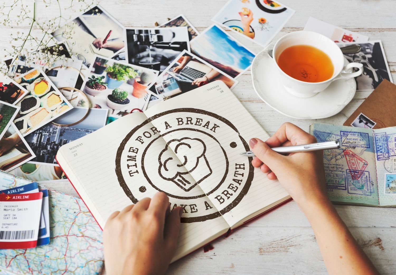 Hands sketching a doodle logo on paper beside tea, photos, and art supplies on a desk