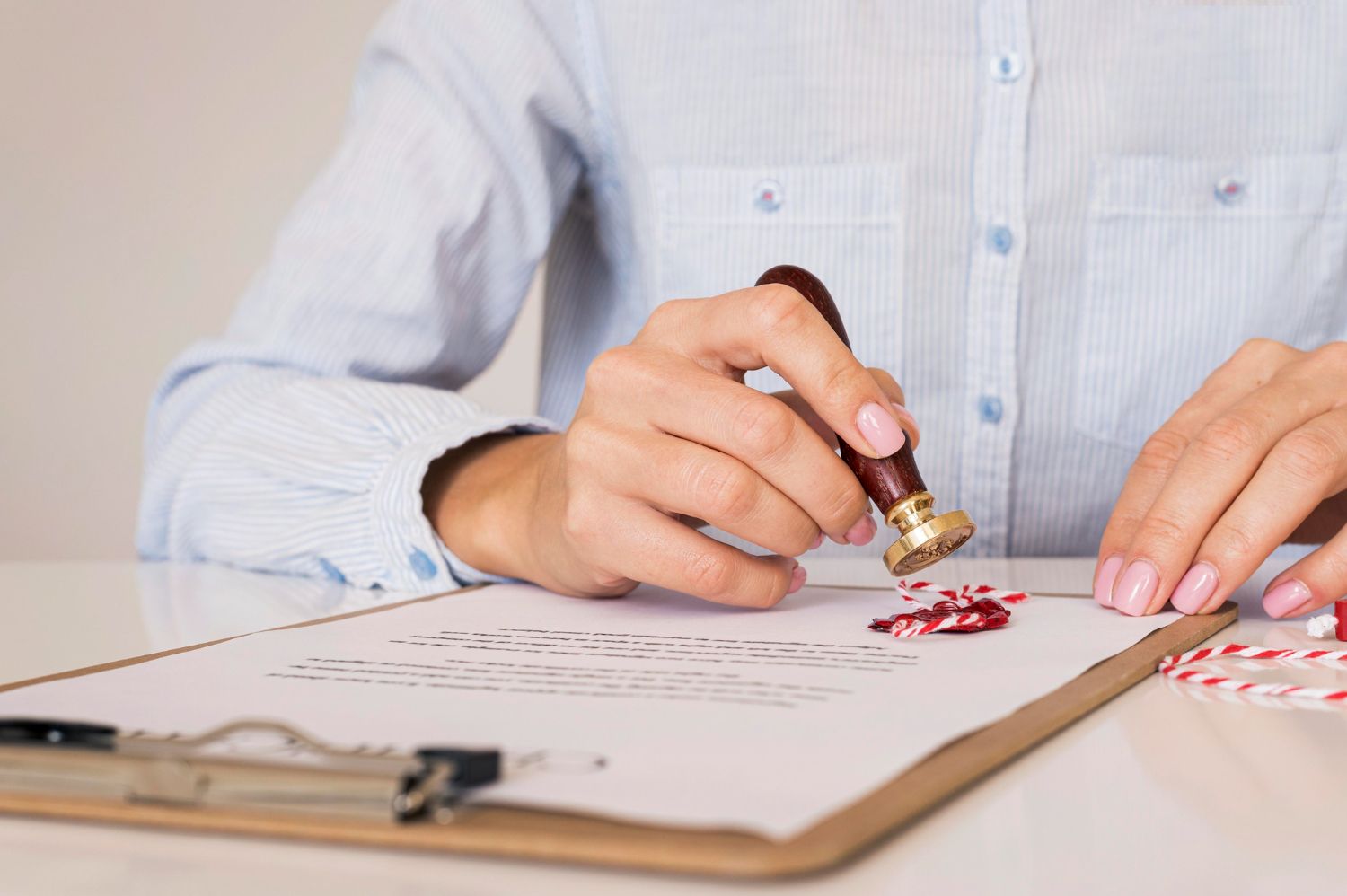 Hands stamping a document on a clipboard with red ink on a desk