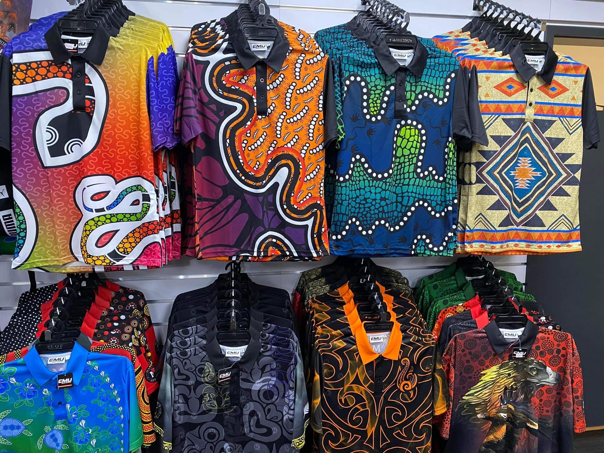 A wall display of colorful polo shirts featuring various vibrant, intricate, and patterned indigenous-style designs.
