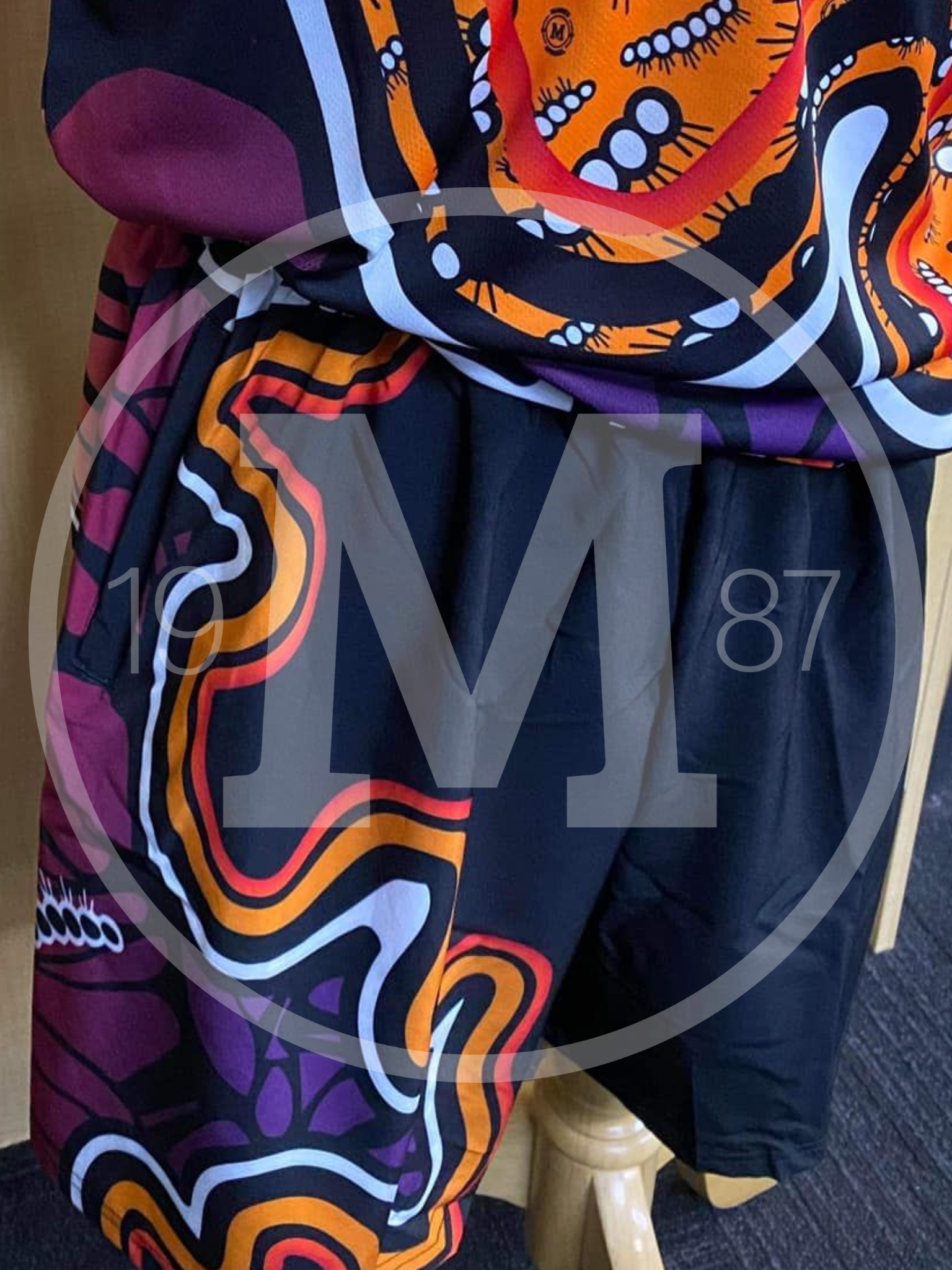 Close-up of a garment with a black, purple, and orange swirling patterned fabric on one side and solid black on the other.