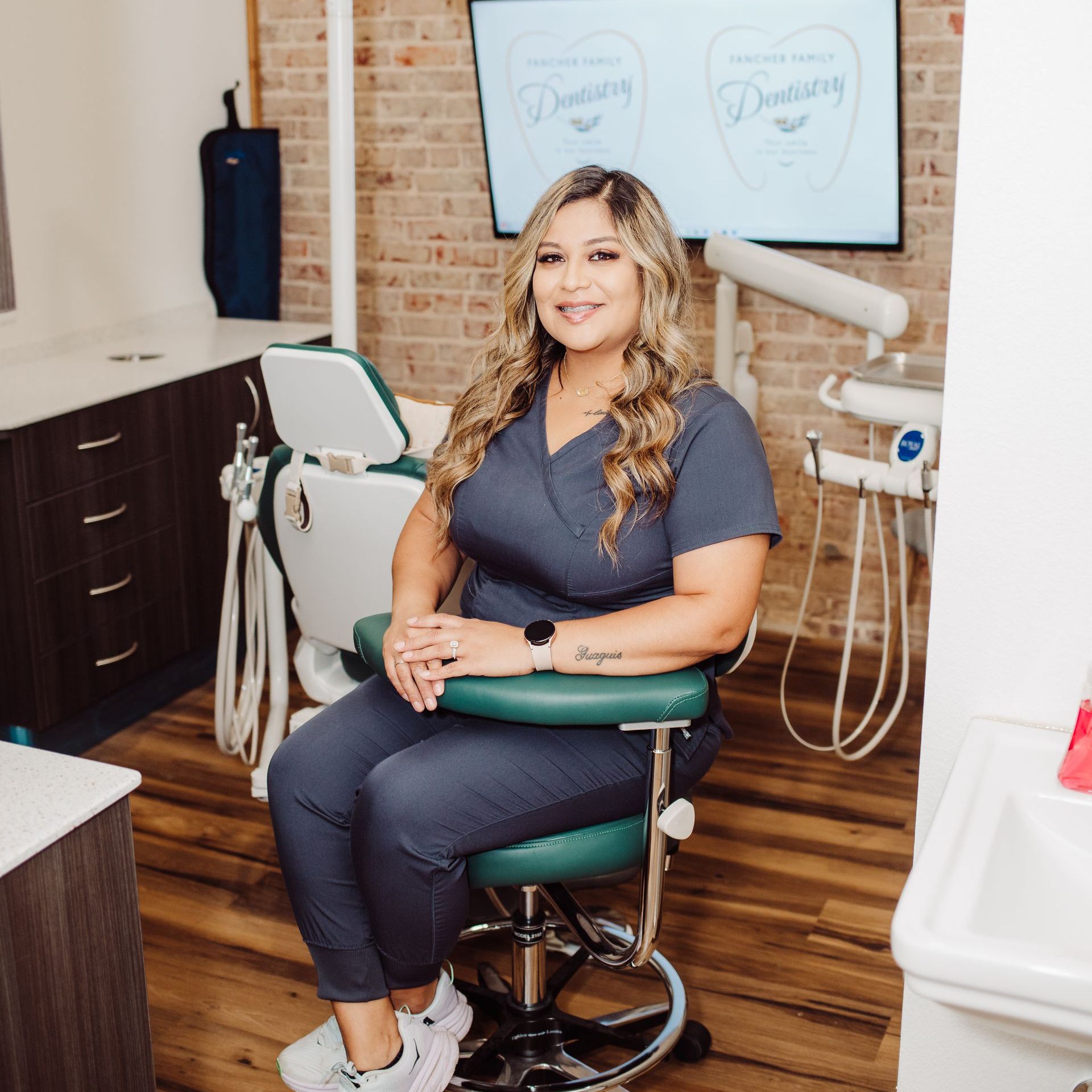 Woman in blue scrubs sits in dental chair in an office setting.